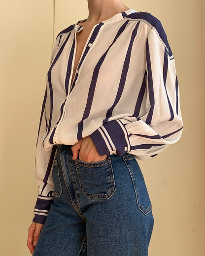A woman wearing a cream-colored long-sleeve button-up blouse with dark navy blue vertical stripes, paired with high-waisted blue jeans.