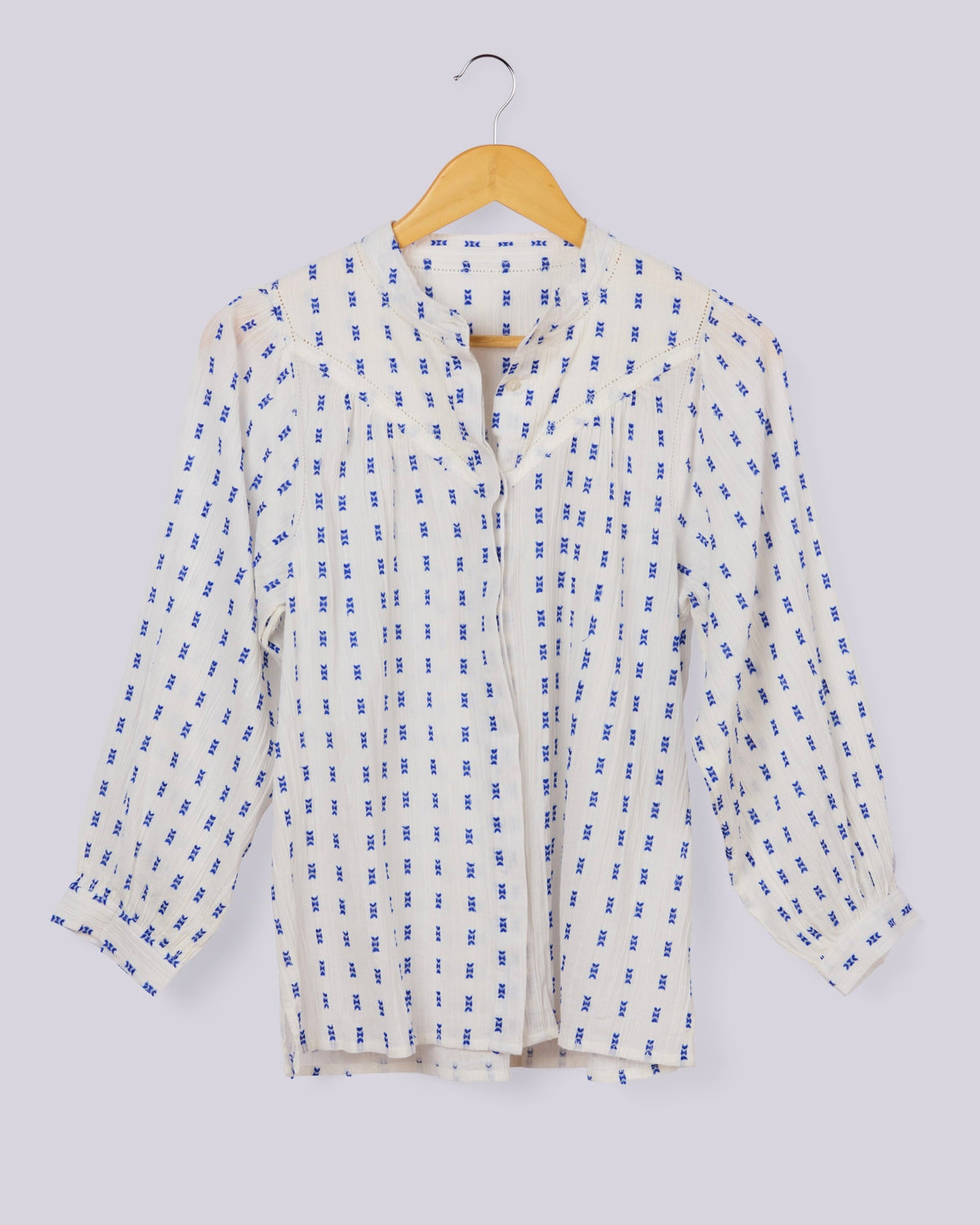 A long-sleeve button-up blouse with a blue and white geometric pattern, hanging on a wooden hanger against a light gray background.