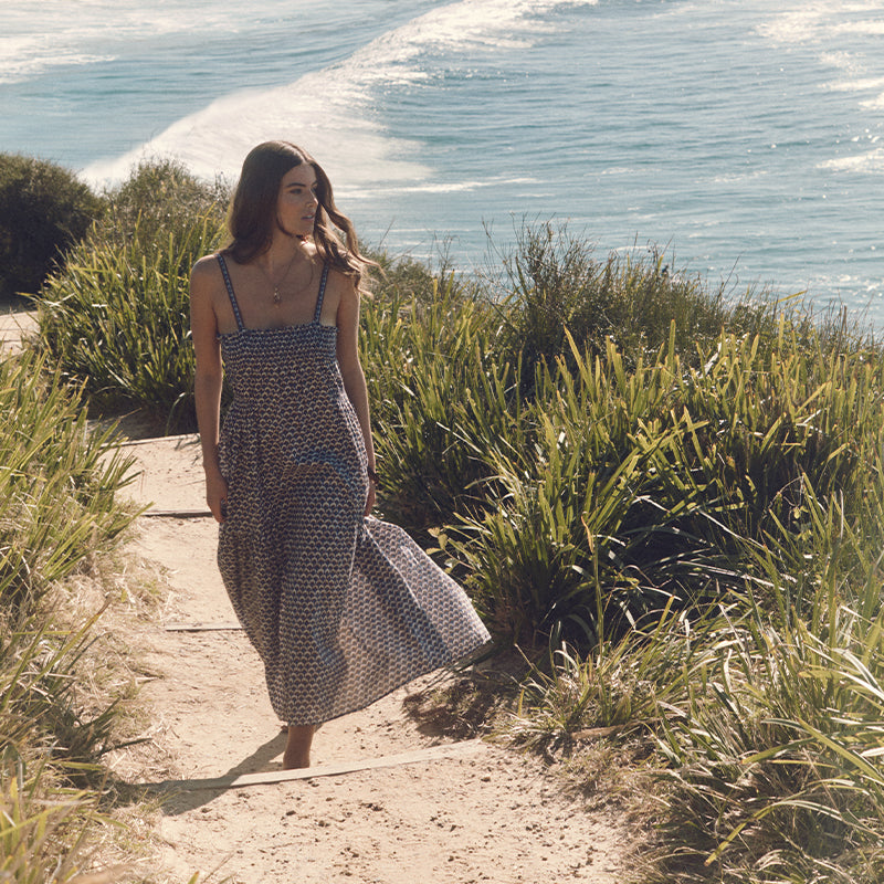 Woman in a long dress walking along a path by the ocean.