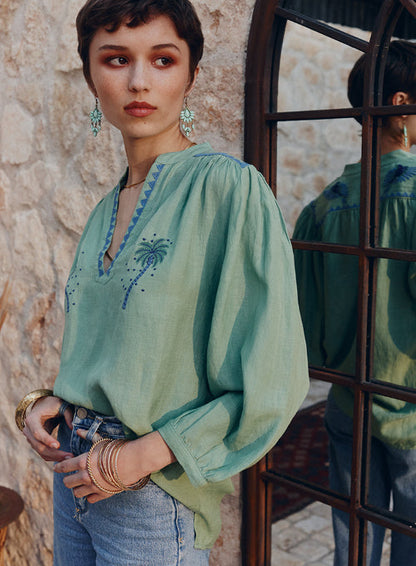 Woman wearing a green embroidered blouse standing against a stone wall.