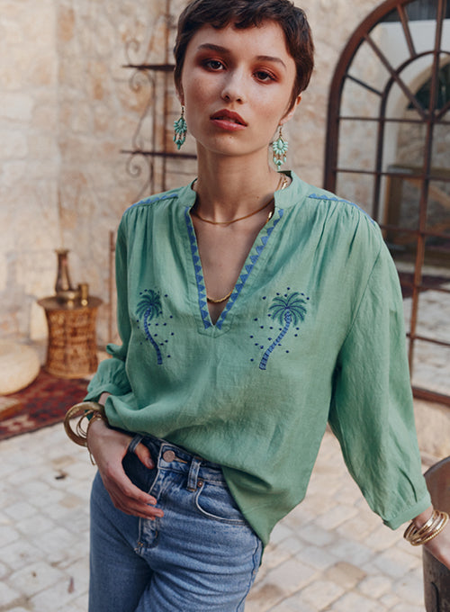 Woman wearing a green embroidered blouse with blue trim in an outdoor setting.
