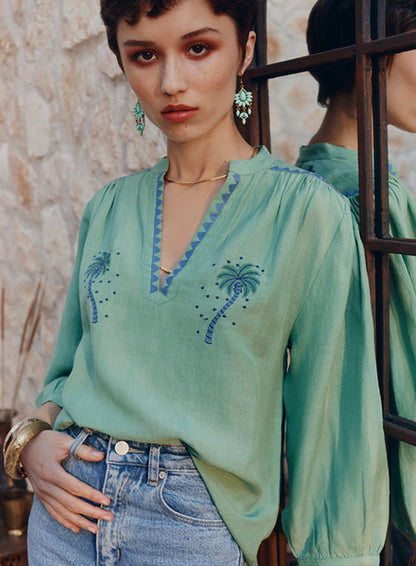 Woman wearing a green embroidered blouse with a stone wall background